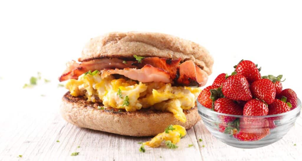 egg sandwich with side of strawberries in a bowl