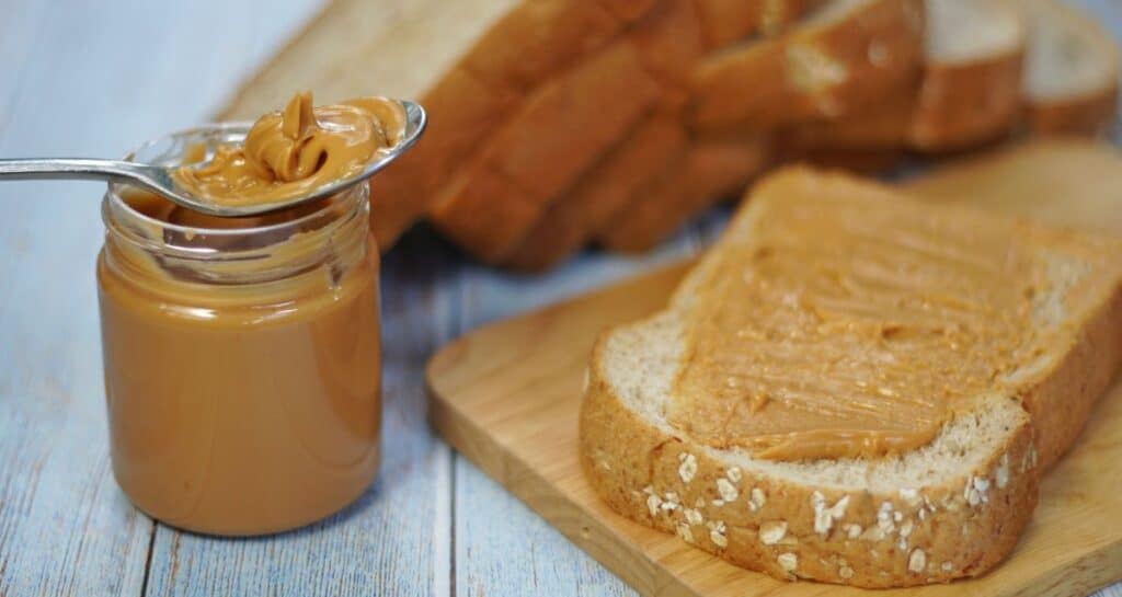 jar of peanut butter and piece of whole wheat high fiber bread with peanut butter spread on it