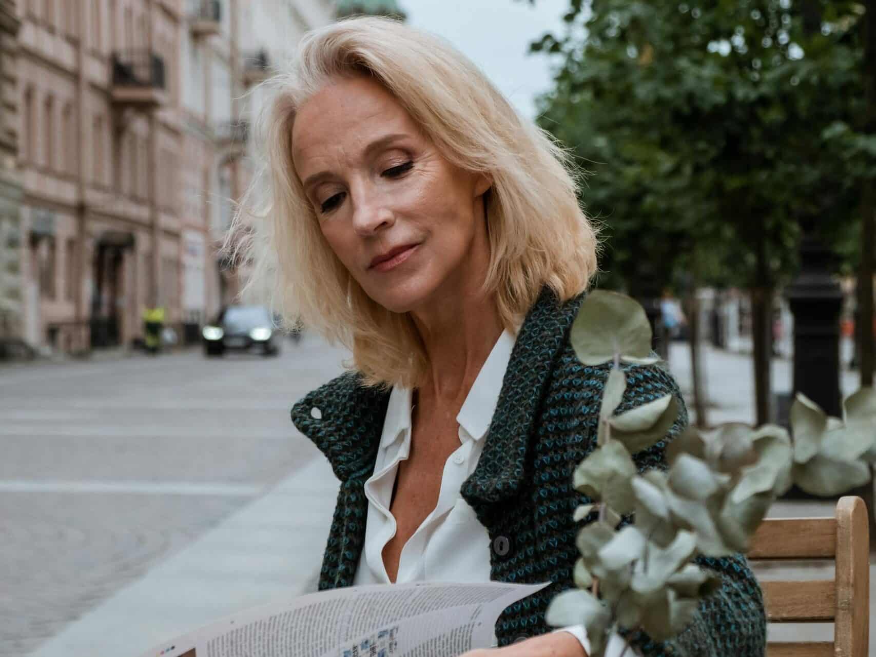 Mature woman reading newspaper at outdoor cafe in city. Summer vibe.